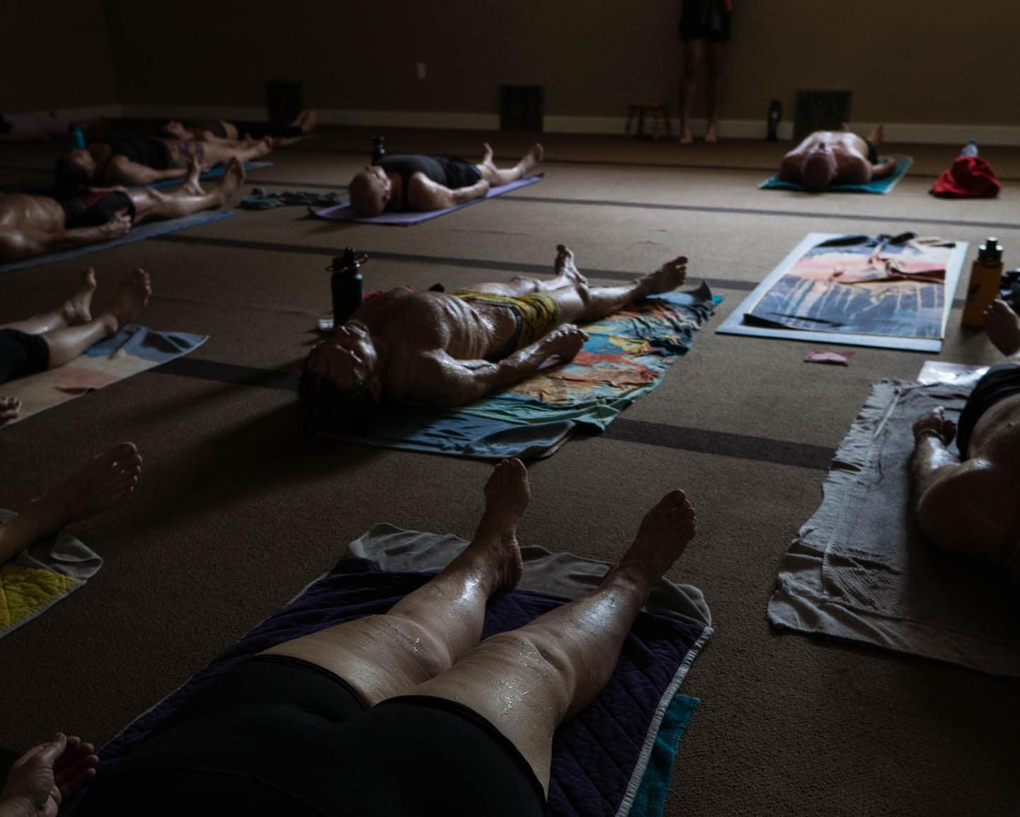 A full class resting in savasana on their mats in the dim, heated room.
