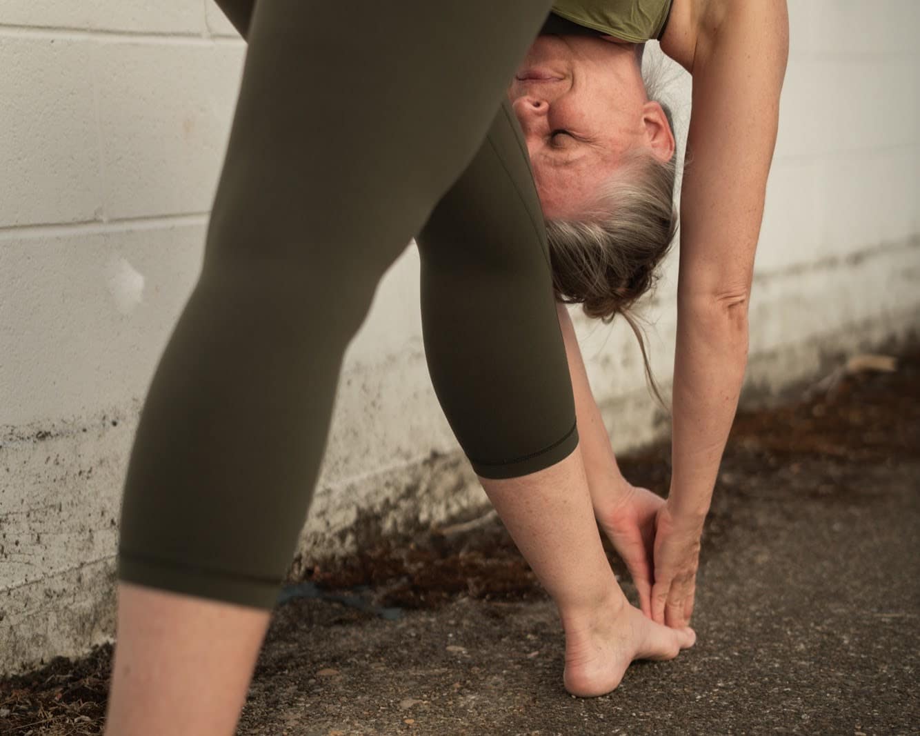 A silver-haired practitioner in a deep standing forward fold.