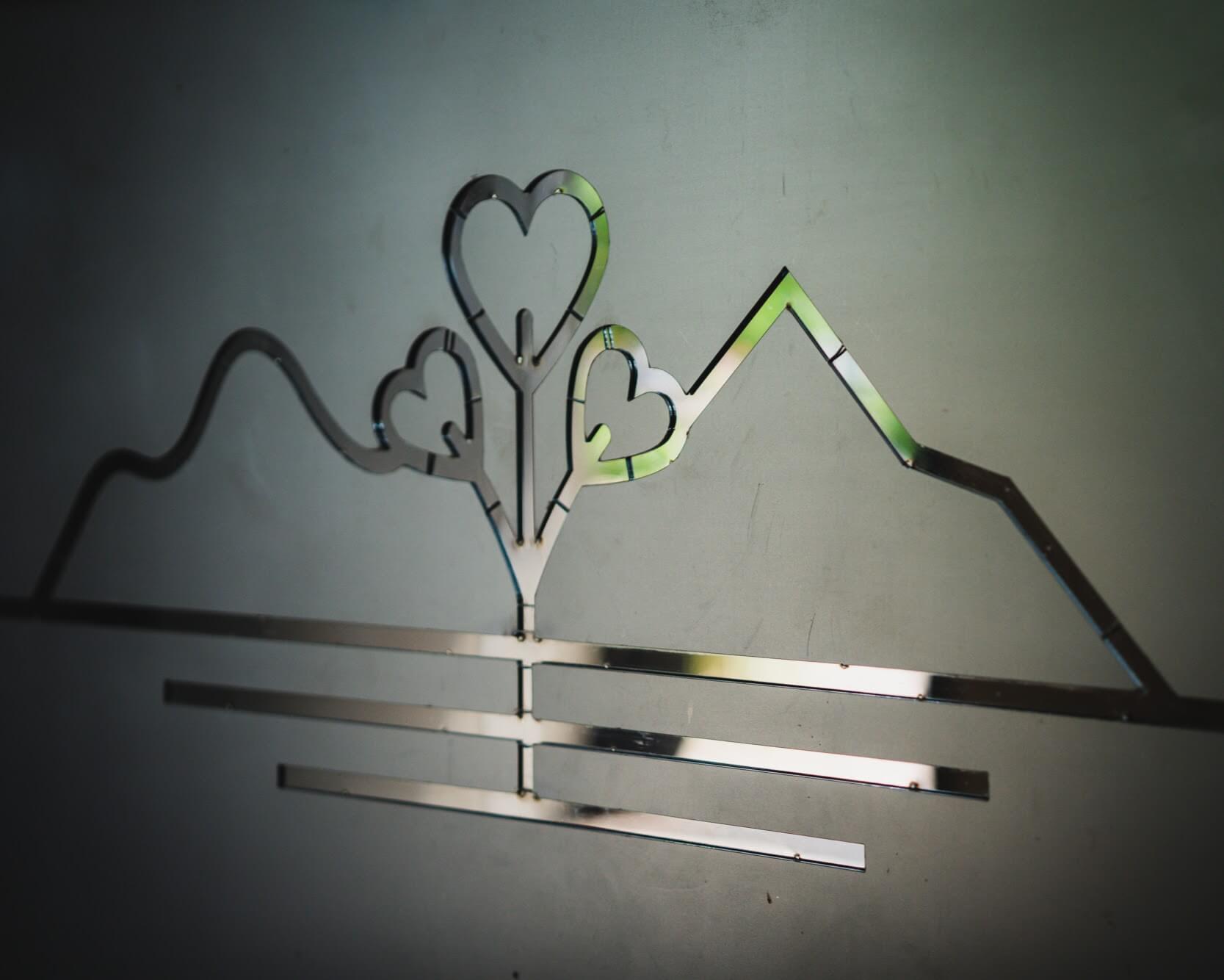 The studio's logo — hearts forming a tree between two mountain ridgelines — cut from polished metal.